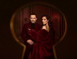 Elegant couple in burgundy outfits posing together inside a keyhole-shaped frame.
